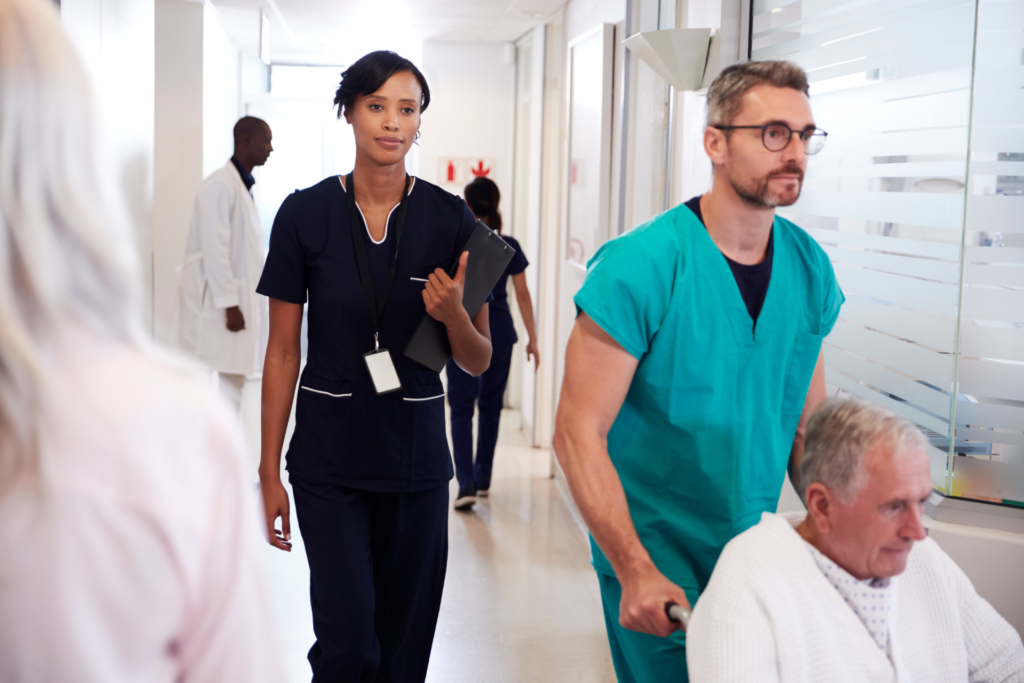 Several Healthcare professionals walking in a hospital hallway. One is pushing a male patient.