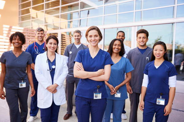 Male and female healthcare professionals standing in front of a building smiling.